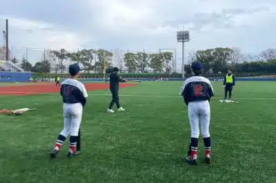 野球場で複数の選手とスタッフが練習している様子を捉えた画像です。バッティング練習が行われており、グラウンドには野球ボールが散らばっています。