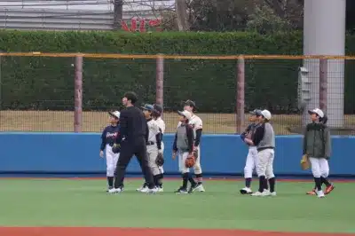 野球場で練習している少年野球チームの子供たちと大人を捉えた一枚。皆、上を見上げたり、話を聞いている様子で、真剣な雰囲気が伝わってきます。