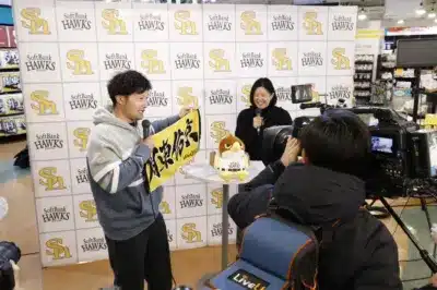 イベントでマイクを持ち話す男性と、カメラマンの様子