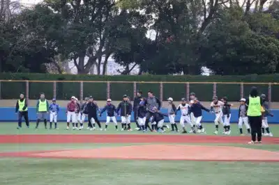 少年野球チームの子供たちが、コーチやスタッフと共に野球場で練習やウォーミングアップをしている様子。様々なユニフォームを着た子供たちが並んで動きを合わせている。