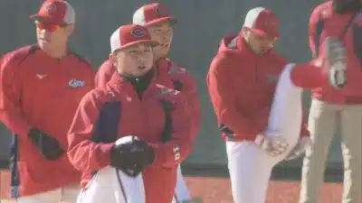 赤いユニフォームと帽子を着用した複数の野球選手が屋外でウォーミングアップや練習をしている様子です。一人の選手は足を上げてストレッチをしており、他の選手たちは見守っています。広島東洋カープの選手たちと思われます。