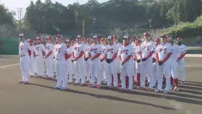 野球のユニフォームを着た大勢の選手またはスタッフが屋外のグラウンドに整列しています。広島カープのロゴが見えます。