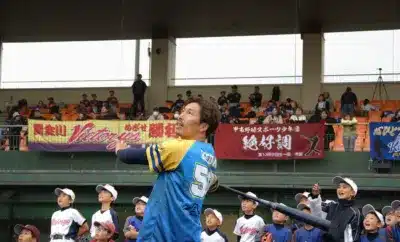 野球場でバットを振る選手と少年野球の子供たち
