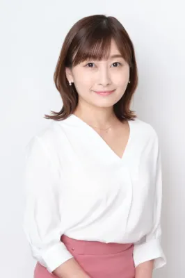 白いVネックのブラウスとピンクのスカートを着用した、肩までの茶色の髪の女性が、優しい笑顔でカメラを見つめているポートレート写真