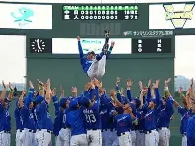 青いユニフォームの野球チームが、選手を胴上げして勝利を祝っている様子。スコアボードには中日ドラゴンズが巨人に大勝したスコアが表示されており、優勝または大きな勝利を収めた喜びが伝わってくる。
