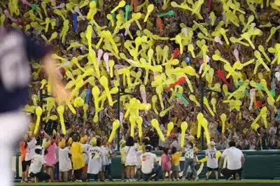 野球場と思われる場所で、多くの観客が黄色い風船を飛ばしている様子