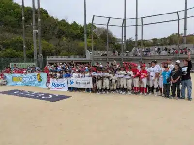 野球場のグラウンドで、大勢の少年野球選手と関係者が集合写真を撮っています。