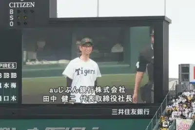 野球場の大型ビジョンに阪神タイガースのユニフォームを着た男性が映し出され、「auじぶん銀行株式会社 田中 健二 代表取締役社長」と表示されている