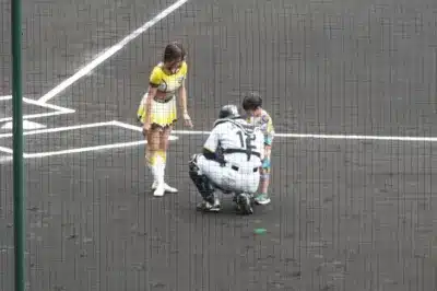 野球場のグラウンドで、黄色のユニフォームを着た女性、野球のキャッチャー、そして子供が交流している様子