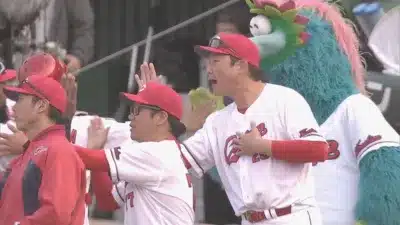 広島東洋カープの選手やコーチらしき男性たちが、球団マスコットと共にグラウンドで応援している様子