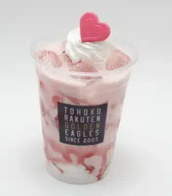 ピンク色のドリンクが透明なカップに入っており、ホイップクリームとピンクのハートの飾りがトッピングされています