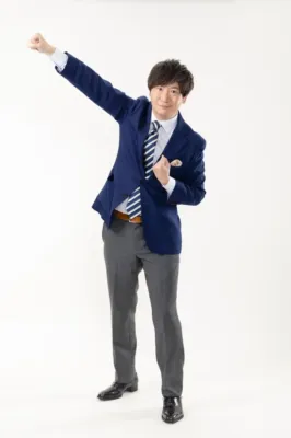 紺色のブレザーとストライプ柄のネクタイを着用した男性が、白背景の前で片腕を高く上げ、ガッツポーズをしている全身写真