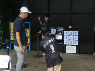 ZOZOマリンスタジアムで開催されていると思われるイベントで、参加者が「ストラックアウト」ゲームを楽しんでいる様子。背番号1「FUJIWARA」のユニフォームを着た人が球を投げようとしており、係員が指示を出している。