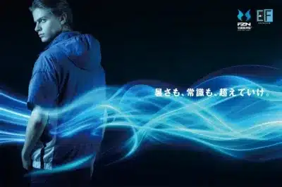 青いジャケットを着た男性が暗い背景に立つ画像。