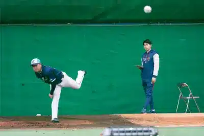室内練習場で投球練習を行う選手と、タブレットでデータを確認する人物