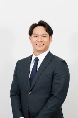 白い背景の前で笑顔で立つ田中広輔氏