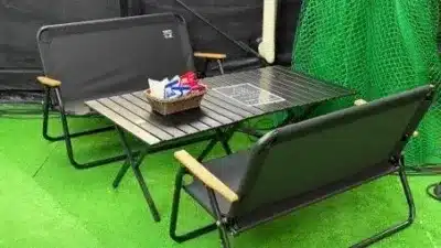 緑の人工芝の上に置かれた、黒い折りたたみ式のアウトドア用ベンチ2脚とテーブルのセット