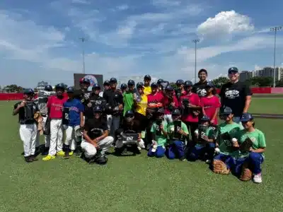 晴れた日の野球場で、ユニフォーム姿の少年野球選手たちとコーチが大勢で集合写真を撮っている