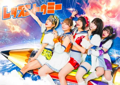 5人の女性アイドルグループが、巨大な鉛筆型のロケットに乗って宇宙を飛び回る、エネルギッシュでカラフルなイメージの画像です。