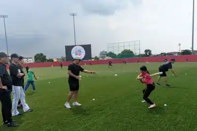 人工芝の野球場で、子供たちが大人から野球またはソフトボールの指導を受けている