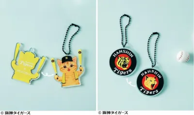 阪神タイガースとネコ部のコラボレーション商品を含む、複数の阪神タイガース関連キーホルダーが並べられています。野球ボールも添えられ、可愛らしい猫のキャラクターが特徴です。