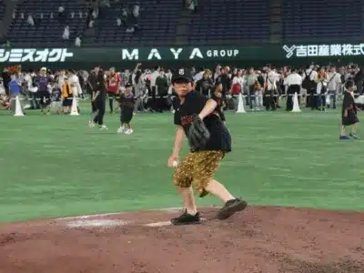 プロ野球スタジアムのグラウンドイベントで、マウンドに立つ少年が野球ボールを投げる瞬間を捉えた一枚。多くの観客が見守る中、子供が真剣な表情で投球フォームに入っている。