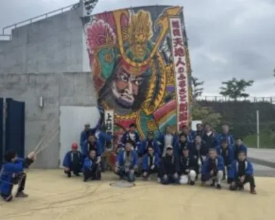 武将が描かれた凧の前で人々が集まる様子