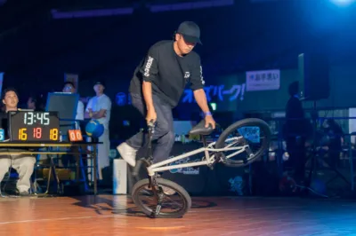 暗い屋内ステージで、男性がBMX自転車でフラットランドのトリックを披露しています