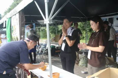 テントの下で行われている屋外イベントで、男性が食べ物を試食している様子