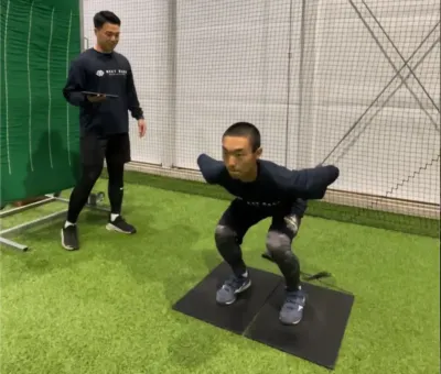 室内トレーニング施設でスクワットをする男性とタブレットを持つコーチ