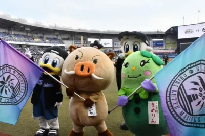 野球場のグラウンドで、千葉ロッテマリーンズのマスコットと地域キャラクター「まめりん」が旗を持って整列している様子