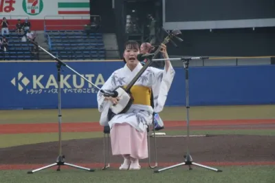 野球場のグラウンドで、浴衣を着た女性が三味線を演奏している様子
