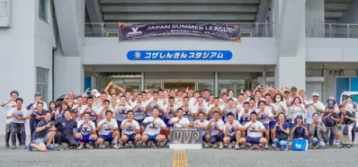 コザしんきんスタジアム前で、大勢の参加者や関係者が集合写真を撮っている様子。多くの人が手でハートマークを作り、JAPAN SUMMER LEAGUEのバナーとJAPAN WINTER LEAGUEのMVPサインが見られる。