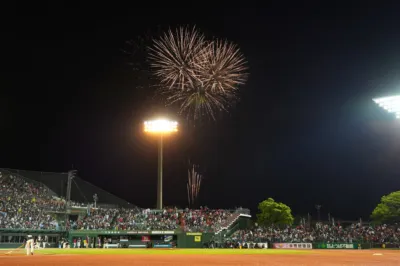 夜の野球場で、満員の観客が見守る中、試合中に打ち上げられる花火